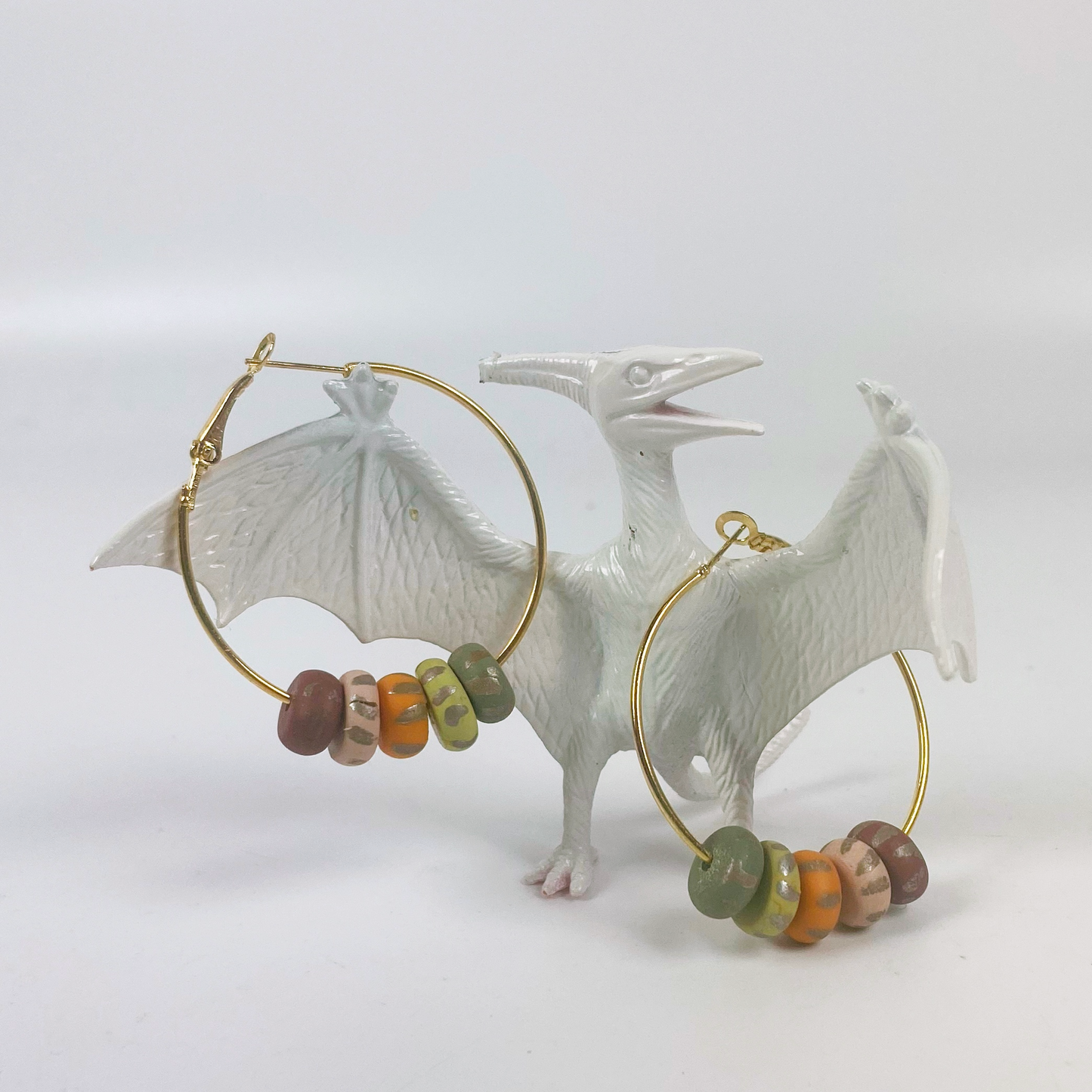 Handmade Polymer Clay Hoop Earrings with Autumn Beads held by a white pterydactyl