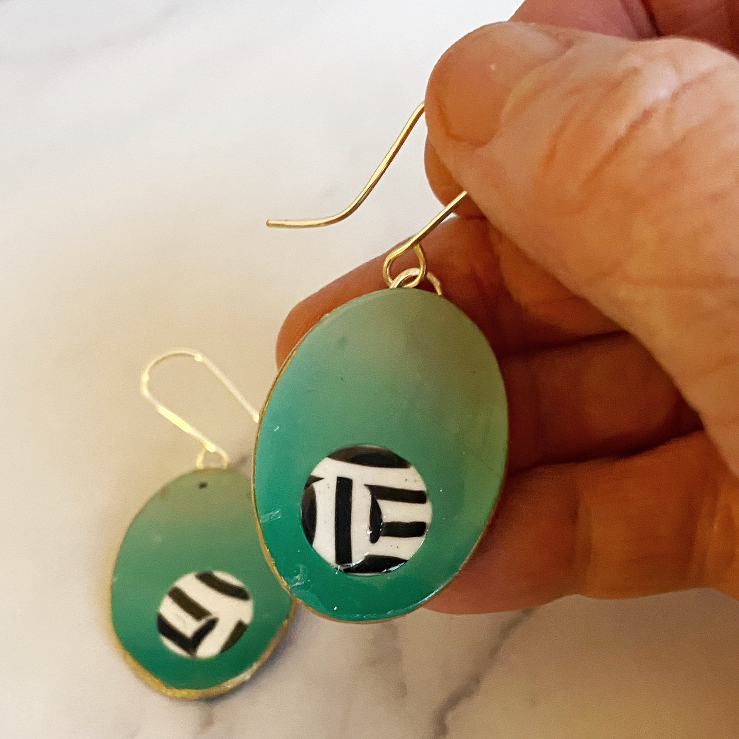 Green earrings with black and white patterns held by a hand on a light background