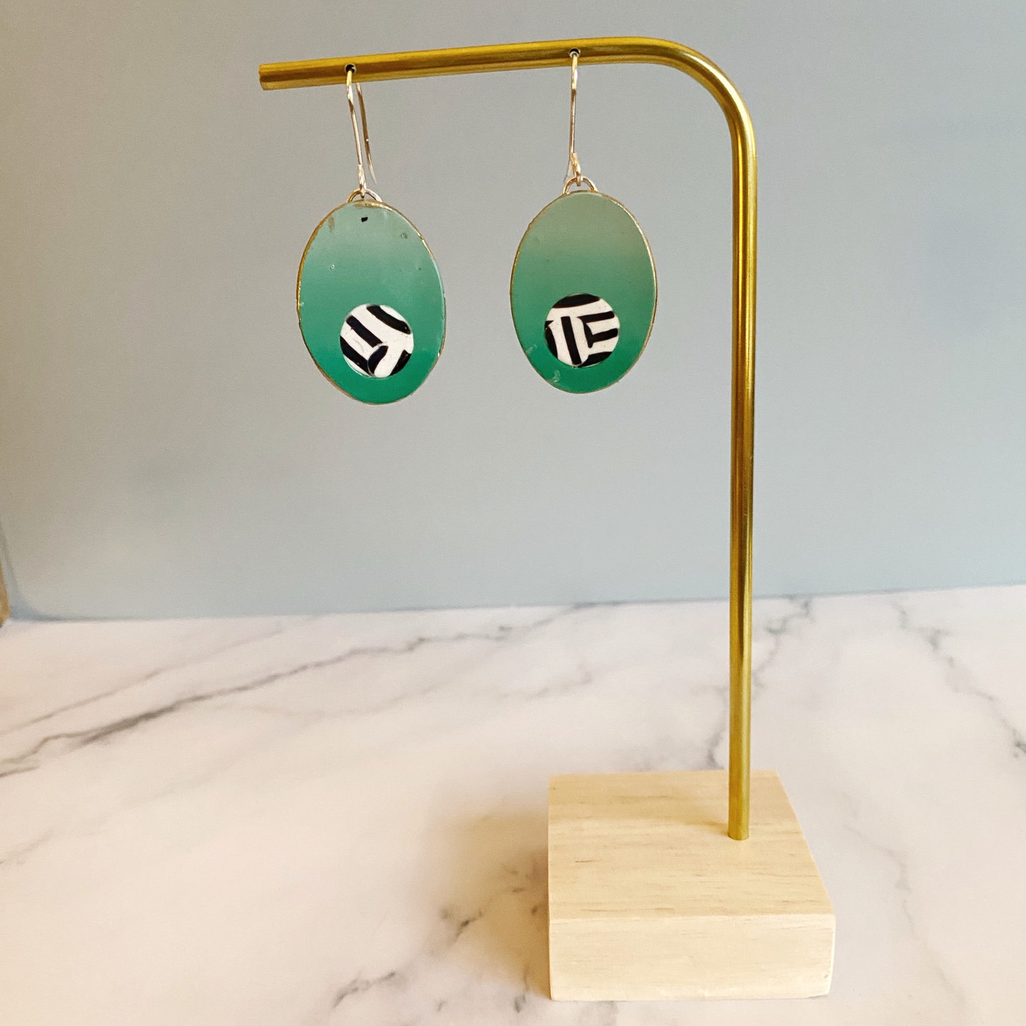 Green gradient earrings with geometric design on a gold stand against a marble surface.