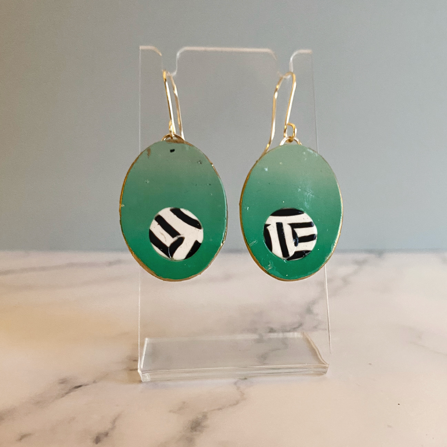 Green oval earrings with zebra pattern centers on a clear stand against a marble background