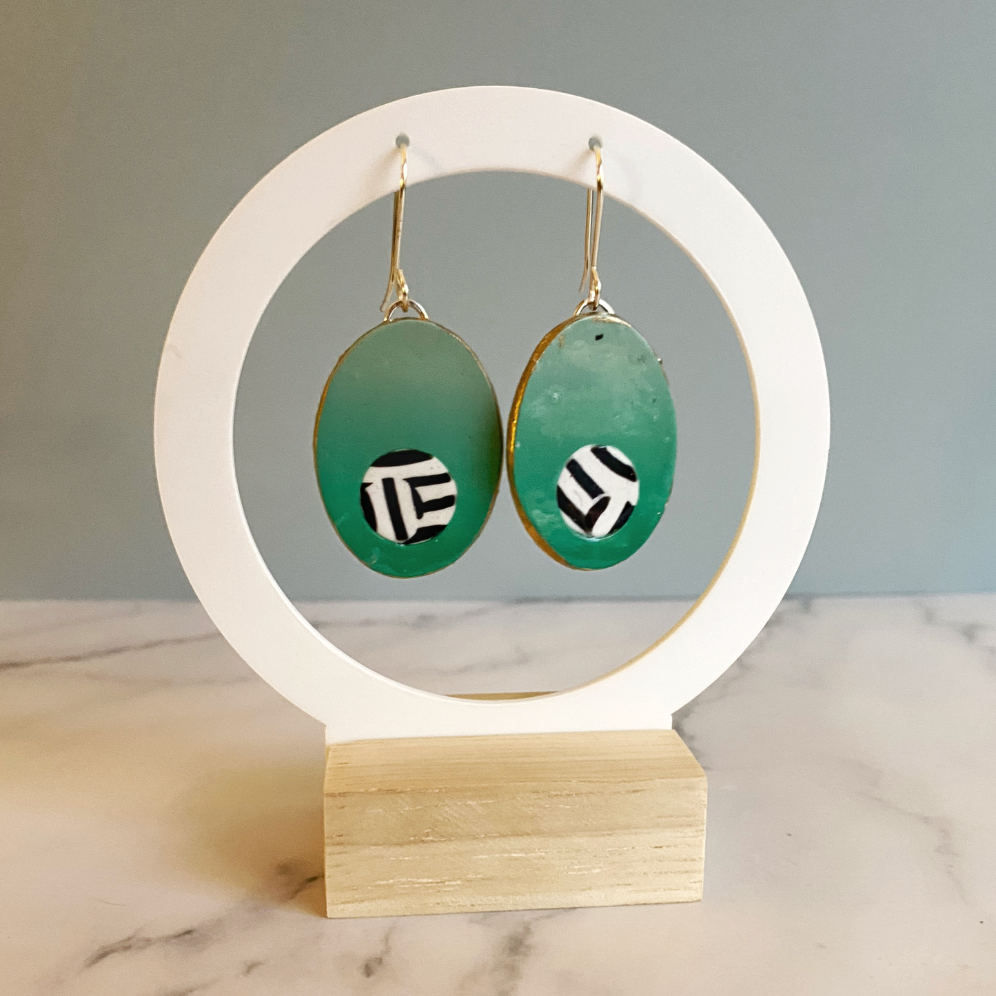 Green earrings with black and white patterns on a wooden stand against a gray background