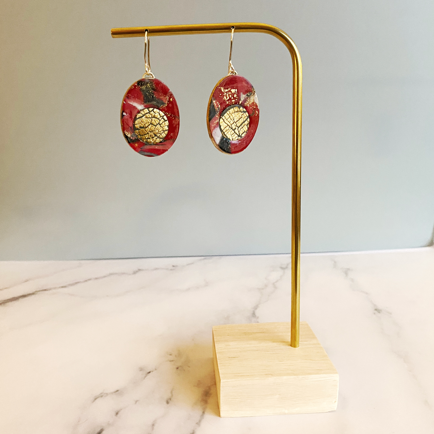 Red Marbled Polymer Clay Earrings with Gold Inset handing from a brass earring stand.