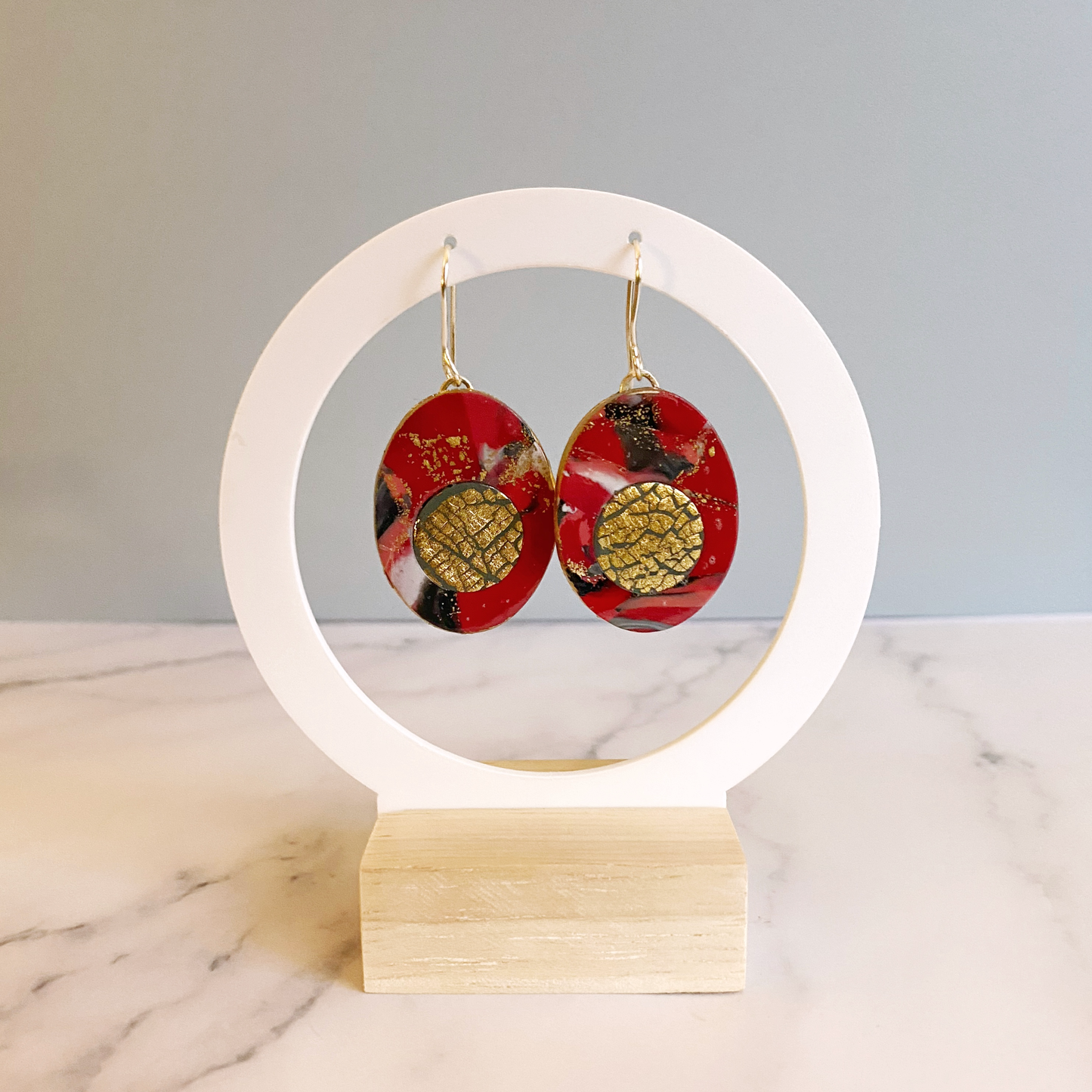 Red Marbled Polymer Clay Earrings with Gold Inset on a white circular display stand.
