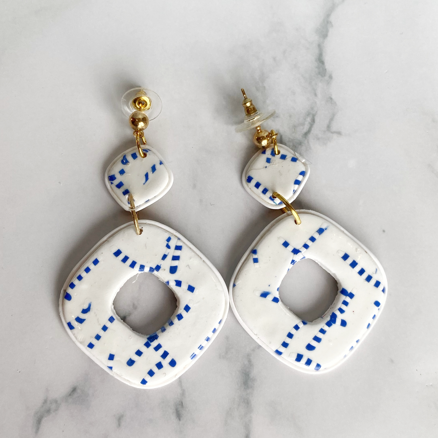 Blue and White Handmade Polymer Clay Square Dangle Earrings laid flat.