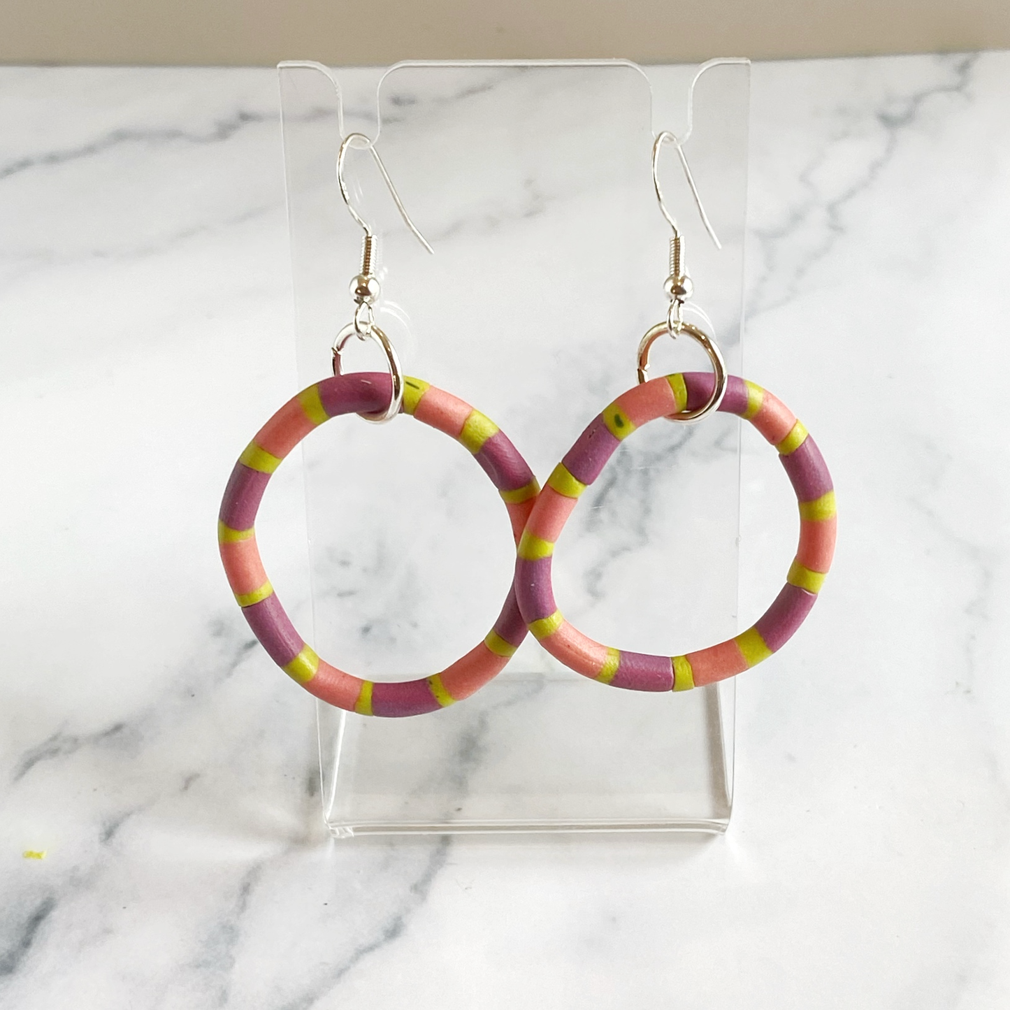 Polymer Clay Rhythm Hoops in Pink, Lavender and Citron on a small acrylic stand.