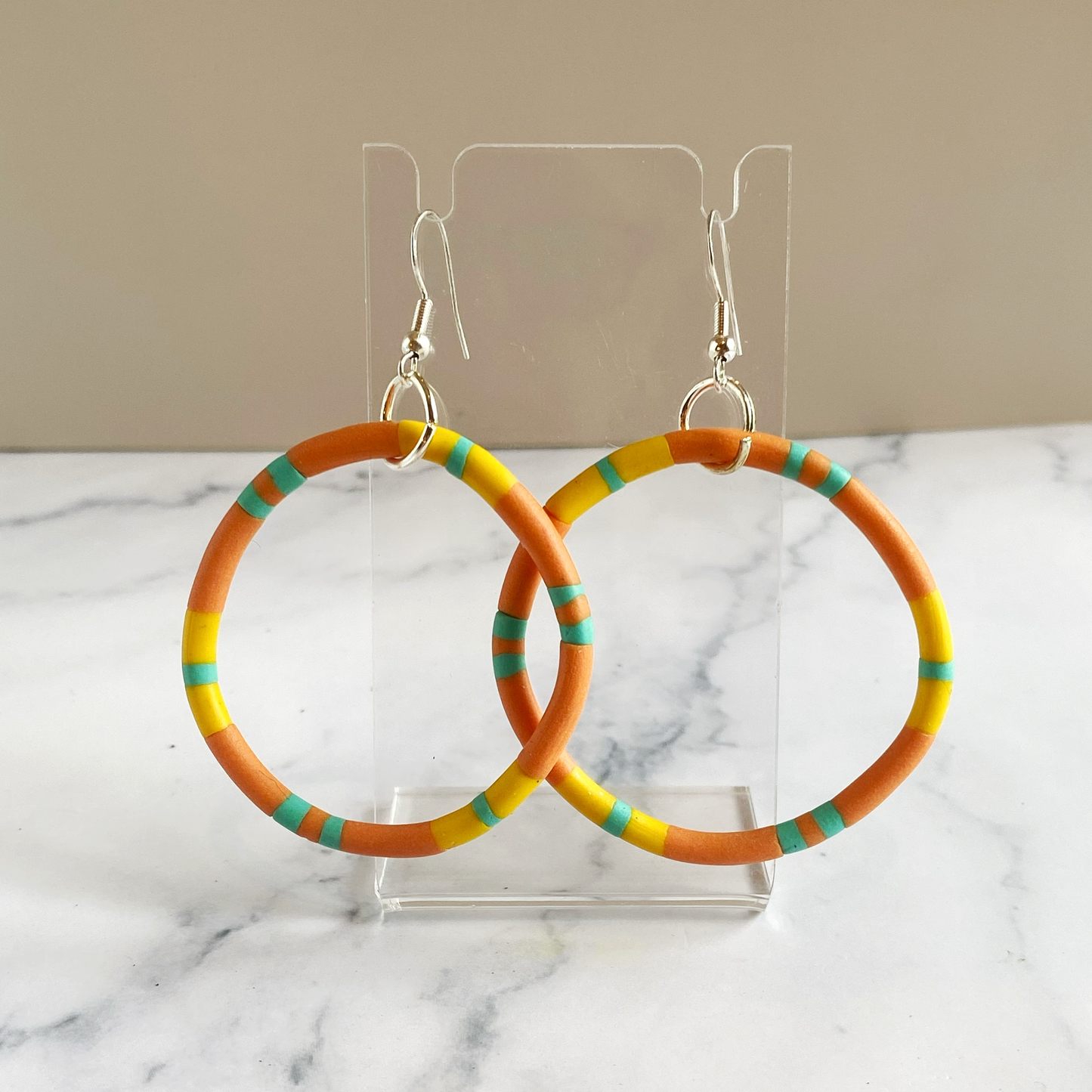 Colorful hoop earrings on a clear stand with a marble background