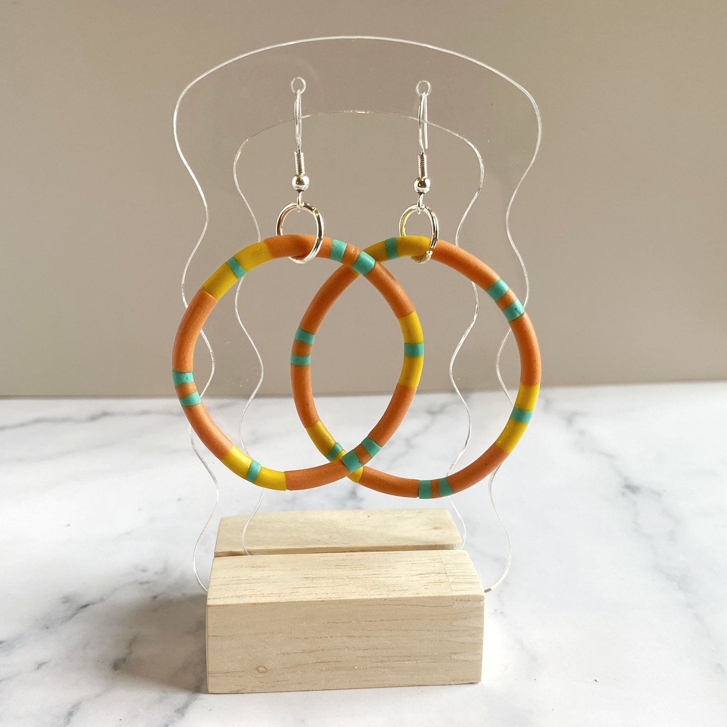 Colorful hoop earrings on a clear acrylic stand with a taupe background