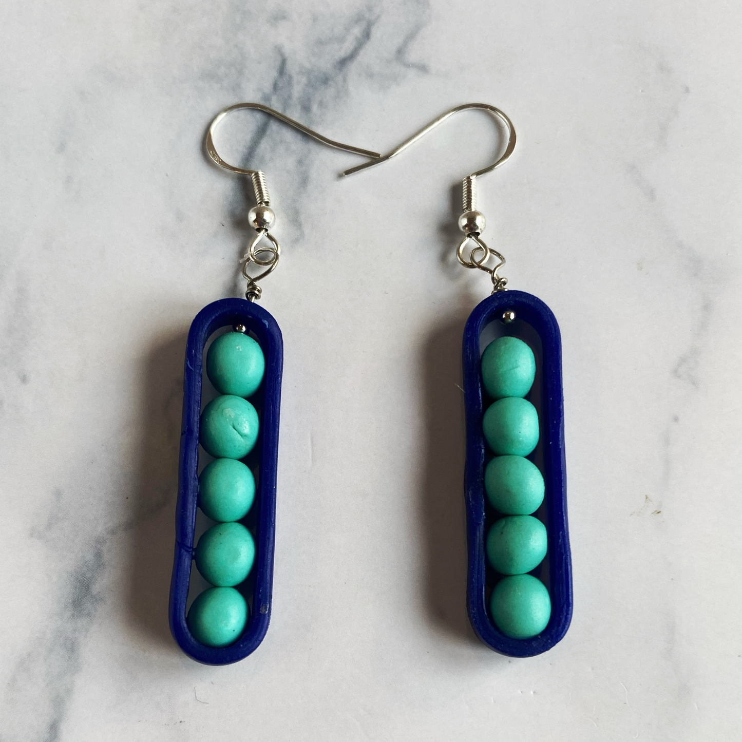 Pair of earrings with blue pods and turquoise beads on a marble background