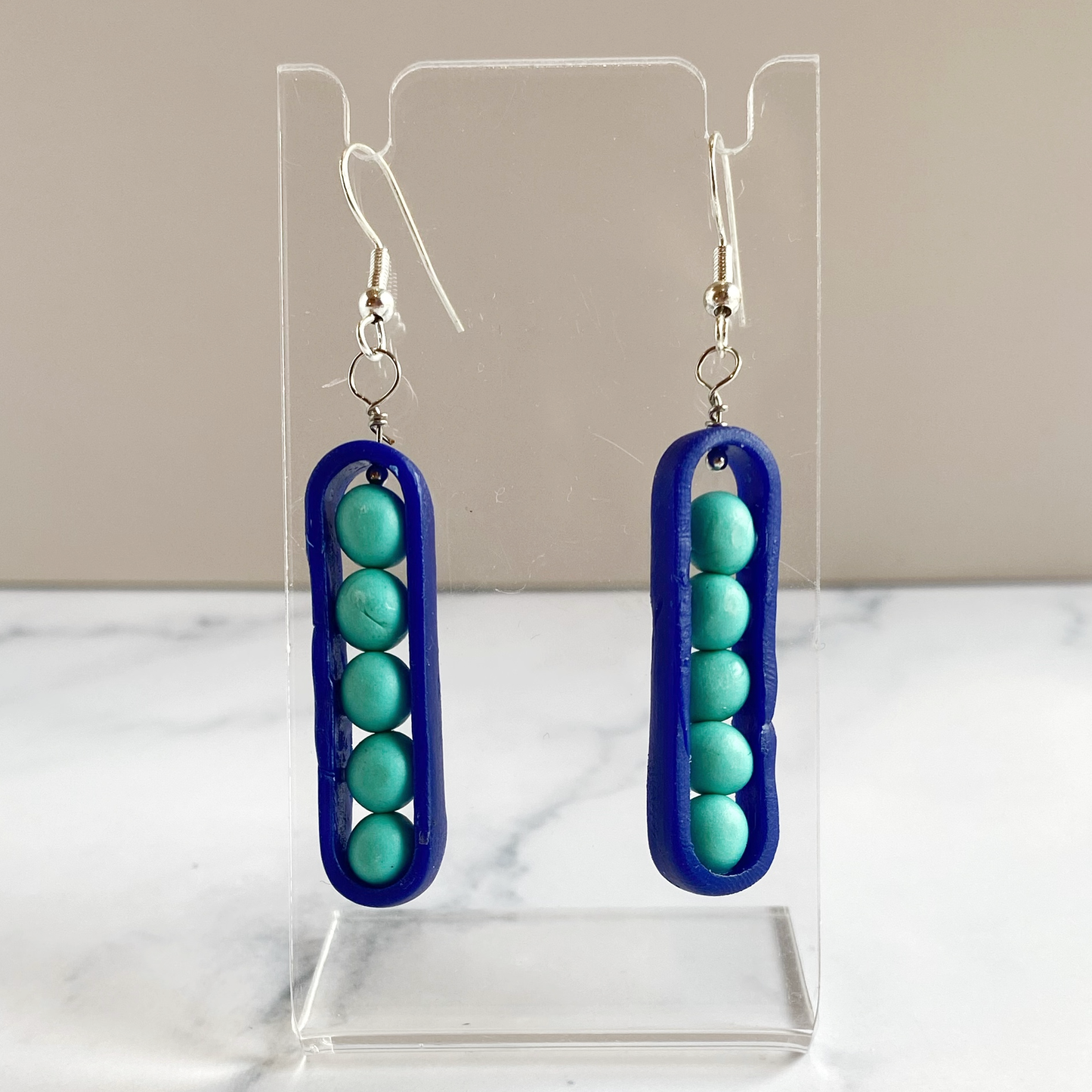 Royal blue and aqua peapodearrings on a clear stand with a neutral background