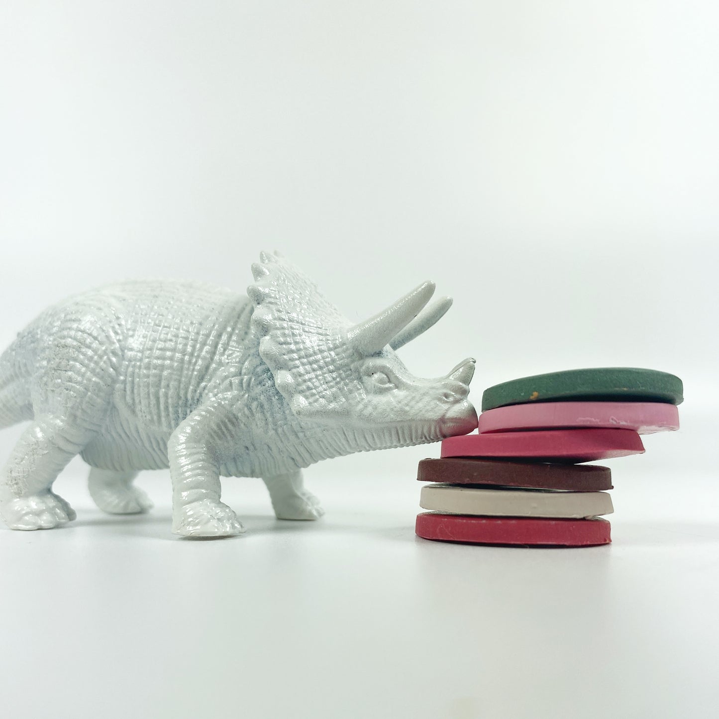 A stack of 6 polymer clay color sample discs with a white dinosaur trying to knock them over
