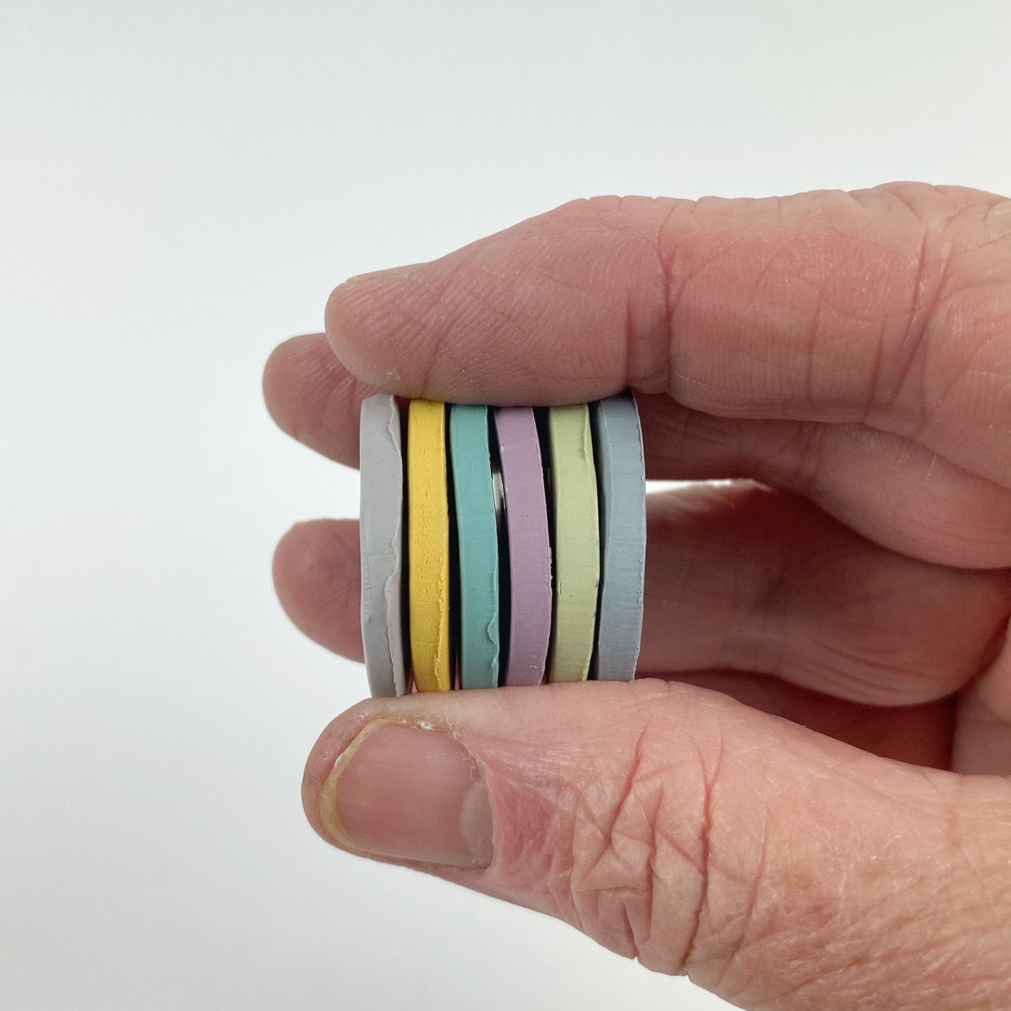 Polymer Clay Secret Admirer Heirloom Harmony. Stacked sample discs of each clay color, held in a hand for a side view