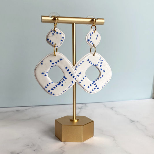Blue and White Handmade Polymer Clay Square Dangle Earrings handing from a brass earring display stand