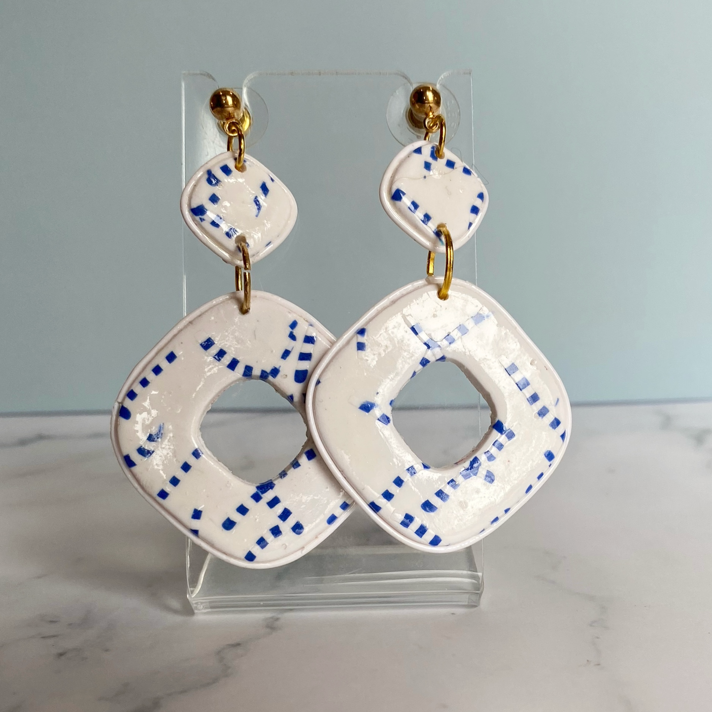 Blue and White Handmade Polymer Clay Square Dangle Earrings on a small acrylic display stand.