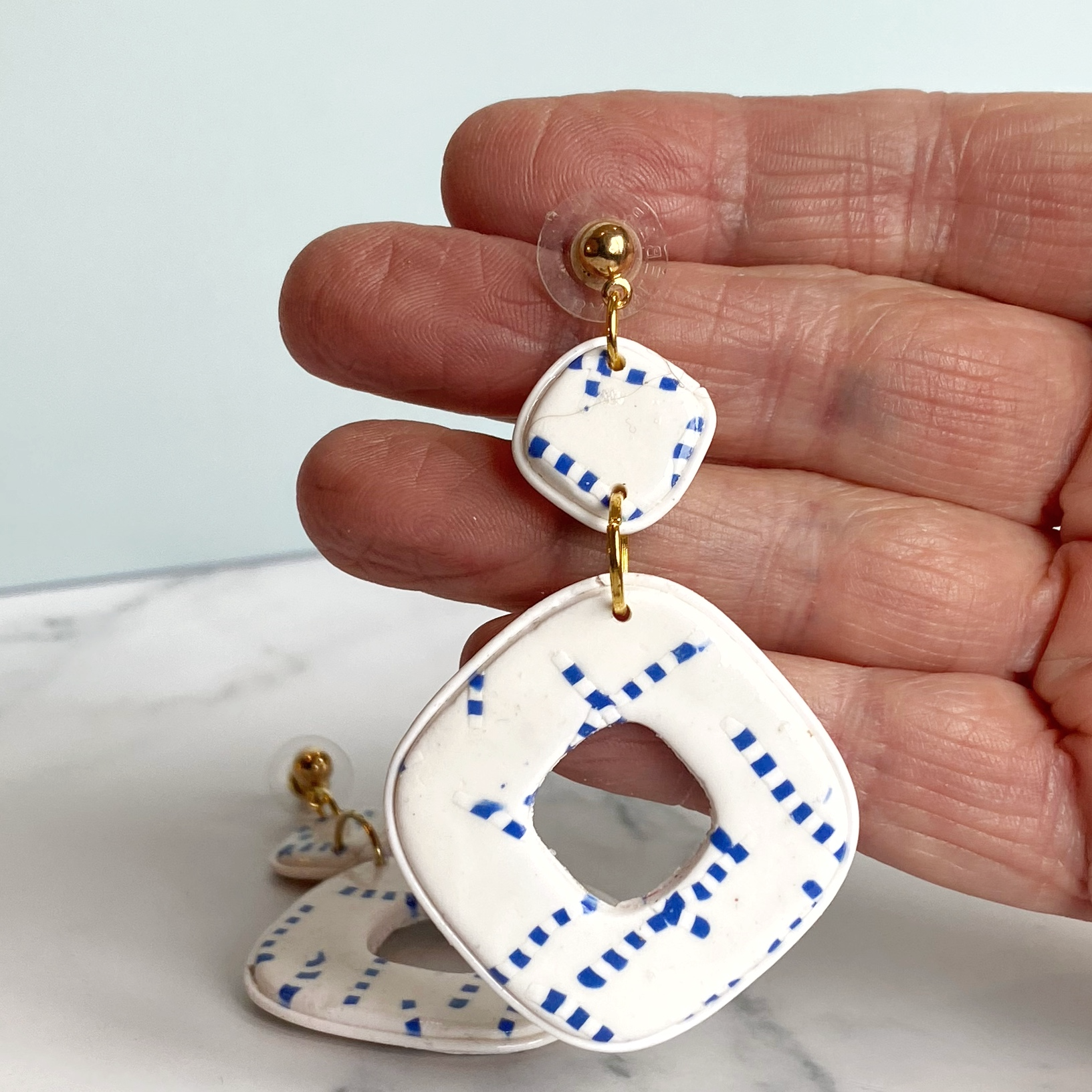 Blue and White Handmade Polymer Clay Square Dangle Earrings hand held for size reference.