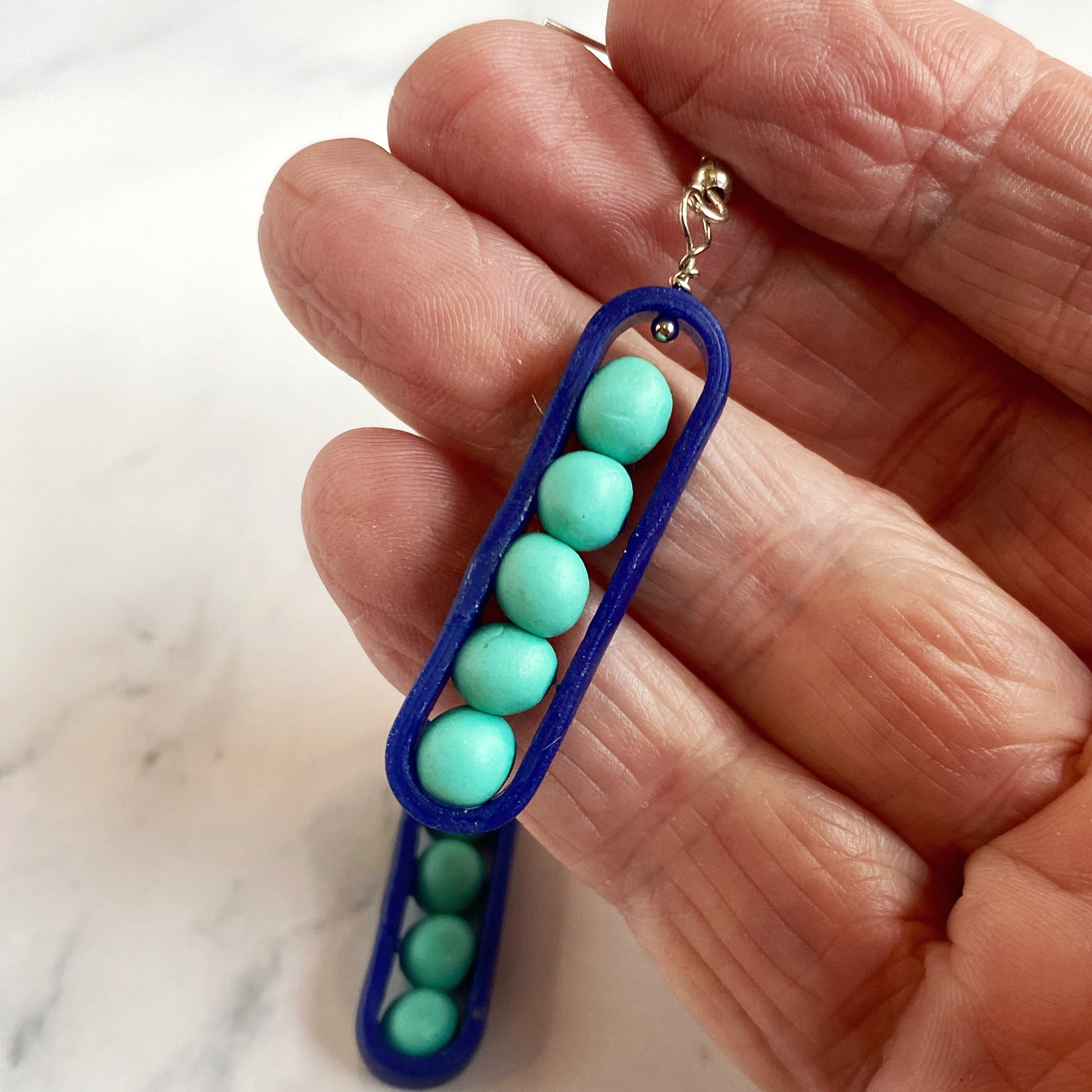 Hand holding an aqua and royal blue  earring against a marble background