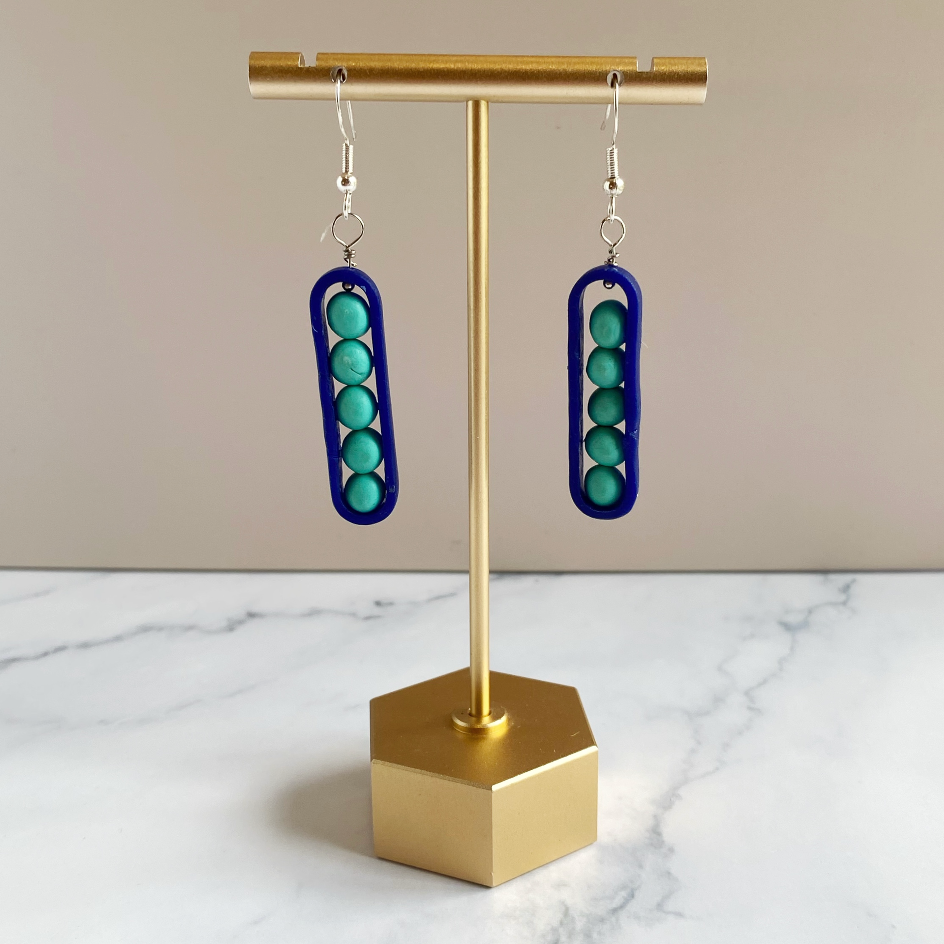 Earrings with royal blue and aqua 'peas'on a brass earring stand against a beige background