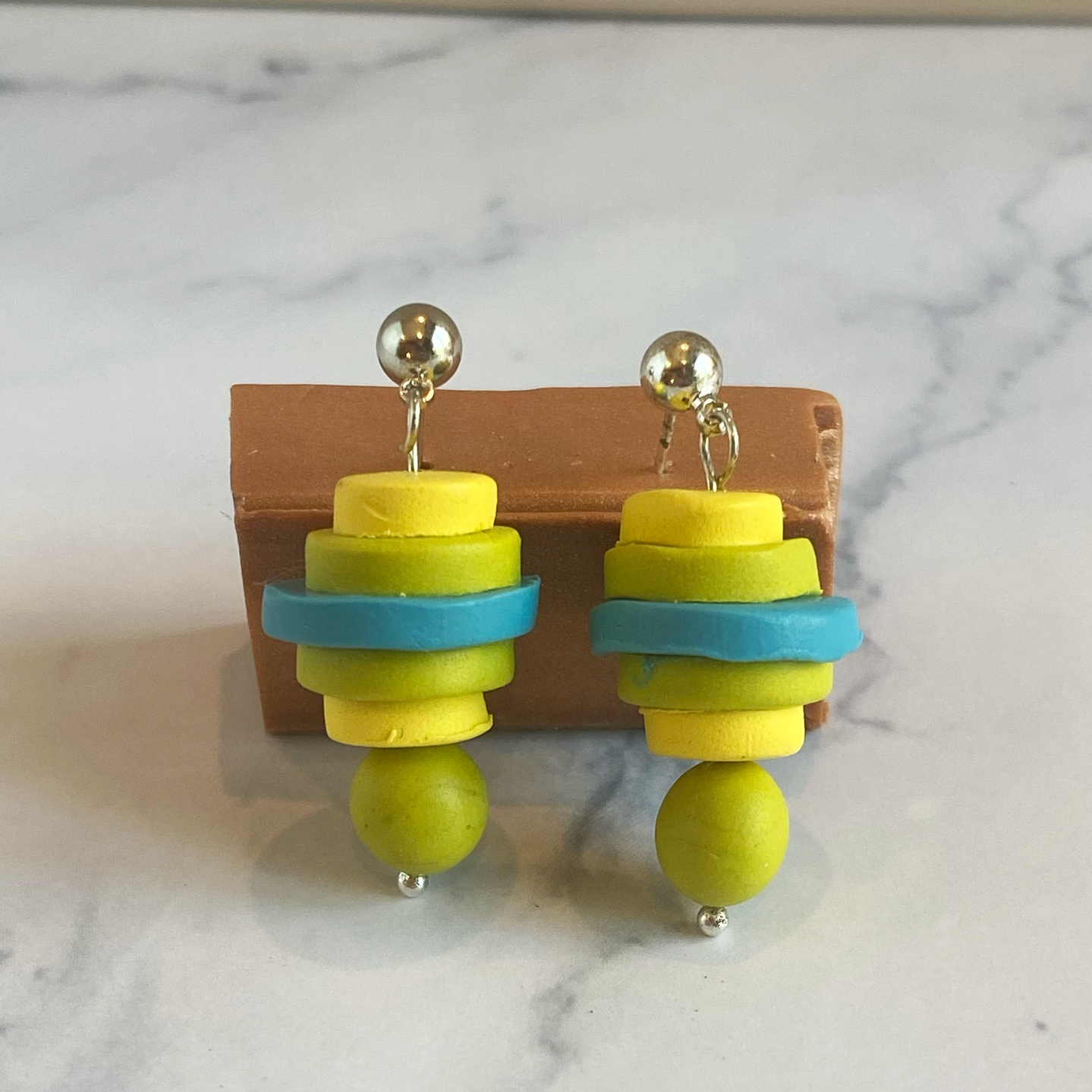 Colorful stacked clay earrings on a wooden stand with a marble background