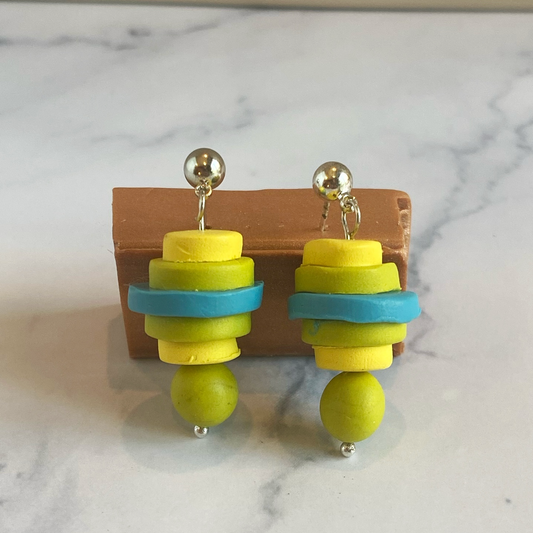 Colorful stacked clay earrings on a wooden stand with a marble background