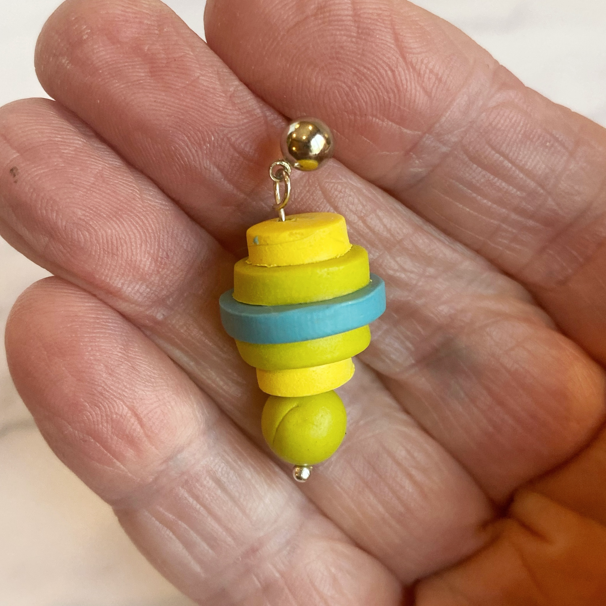 Earring of stacked discs of polymer clay, handheld for size reference