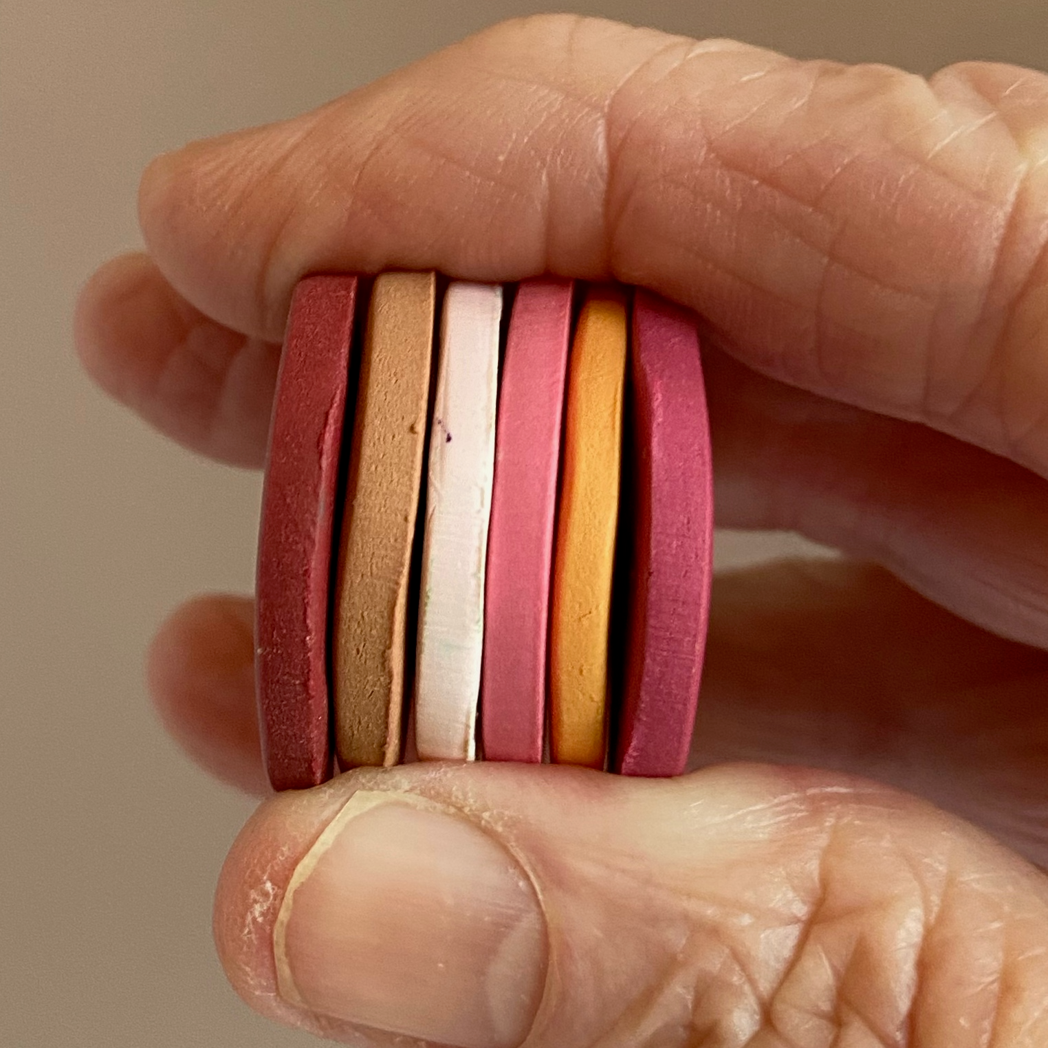 A hand holding sample clay discs in the six colors of this palette.