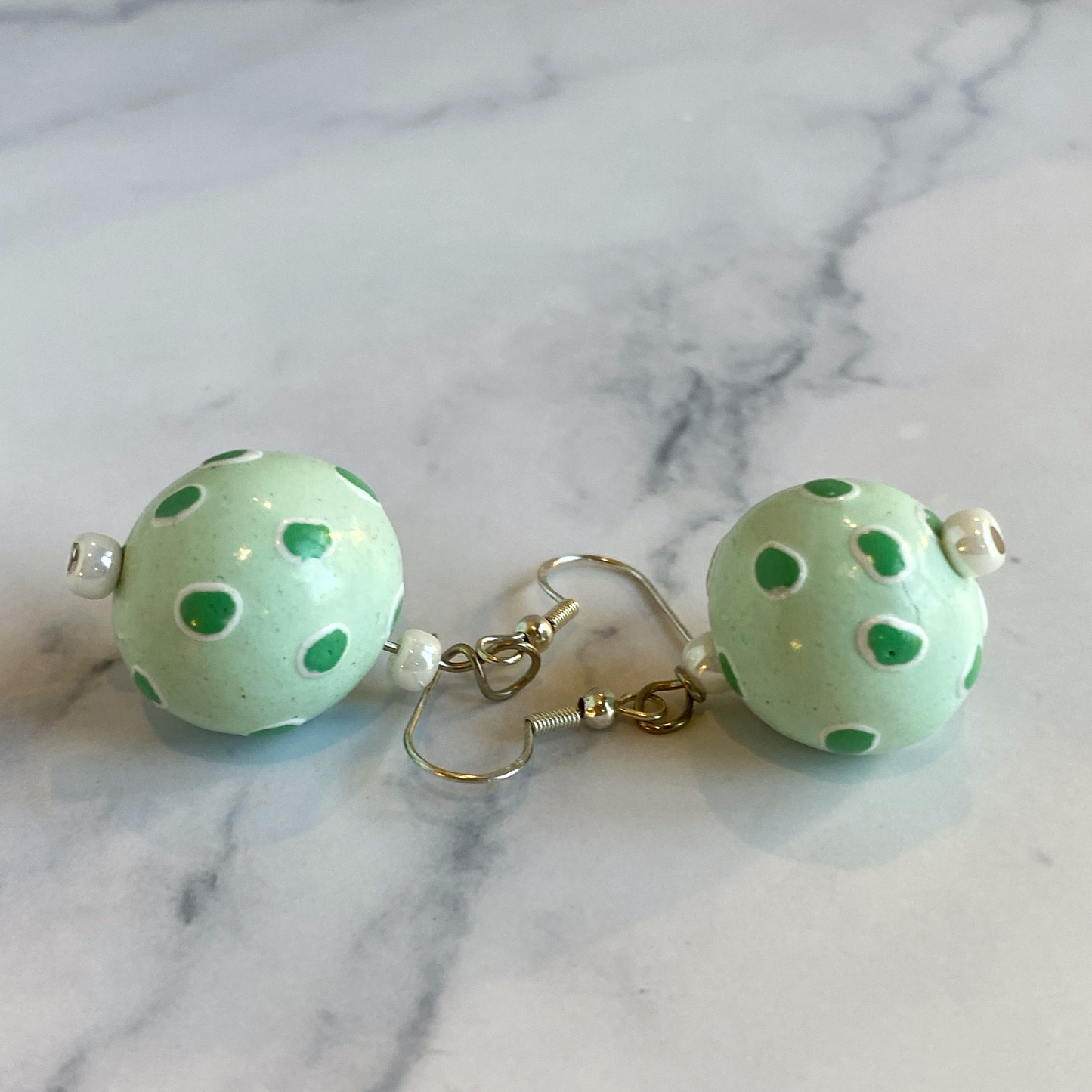 Green polka dot earrings on a marble background