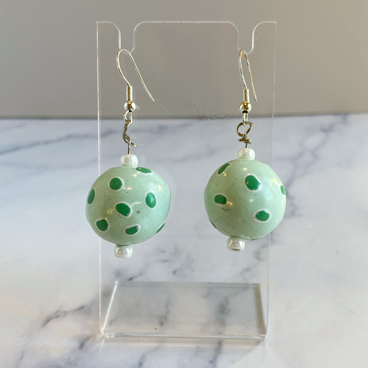 Green polka dot earrings on a clear stand with a marble background