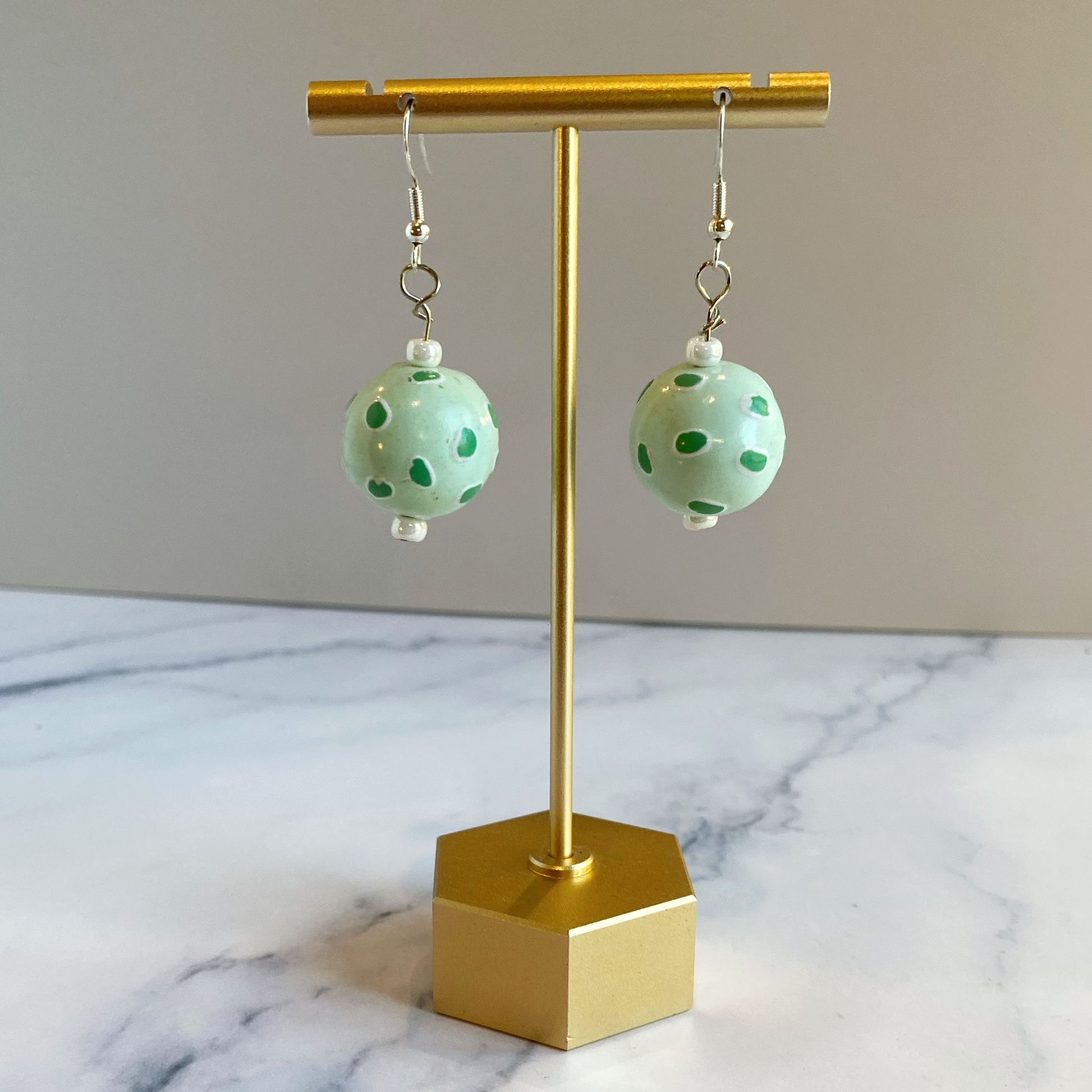 Green polka dot earrings on a gold earring stand with a marble background