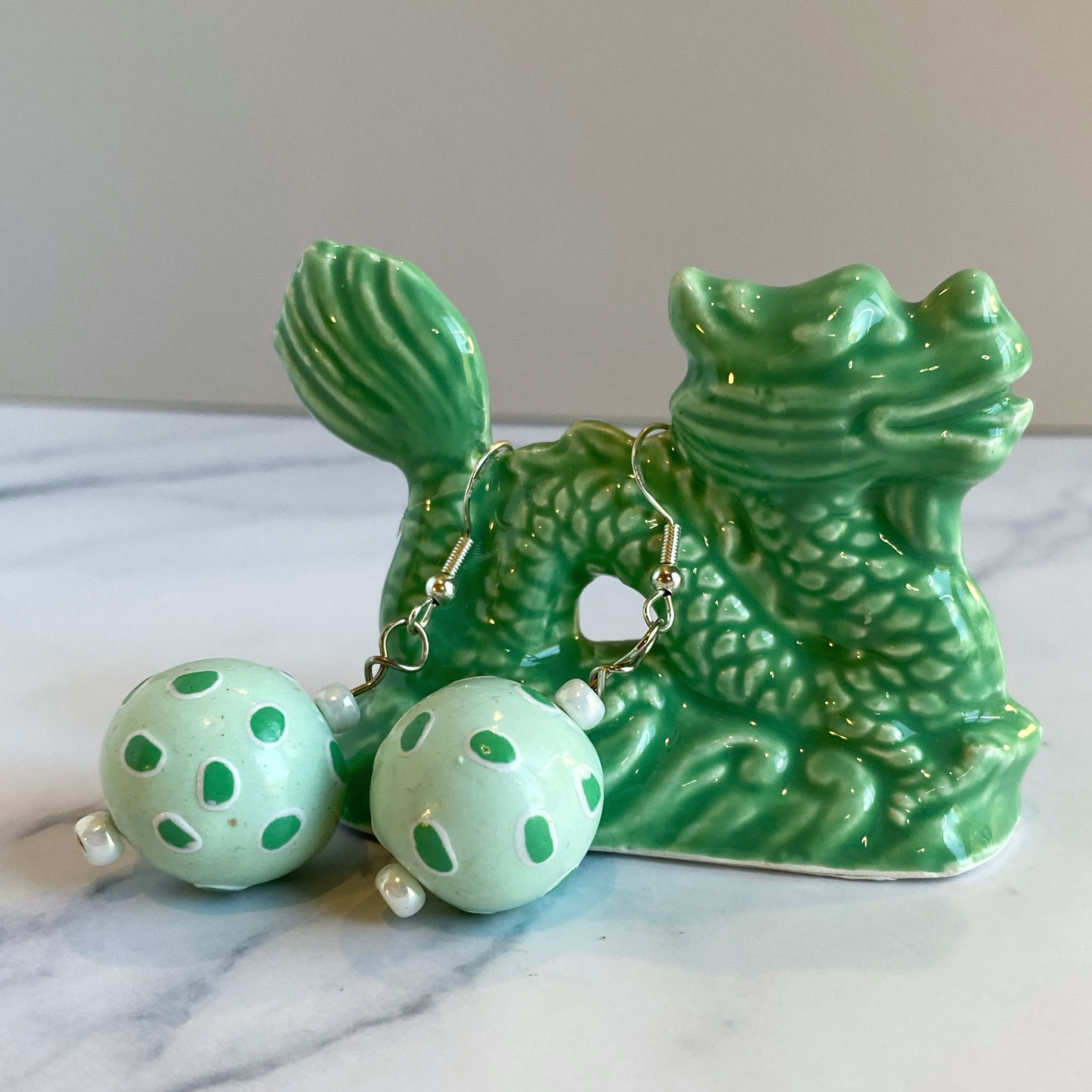 Green ceramic dragon with green polka dot earrings on a marble surface