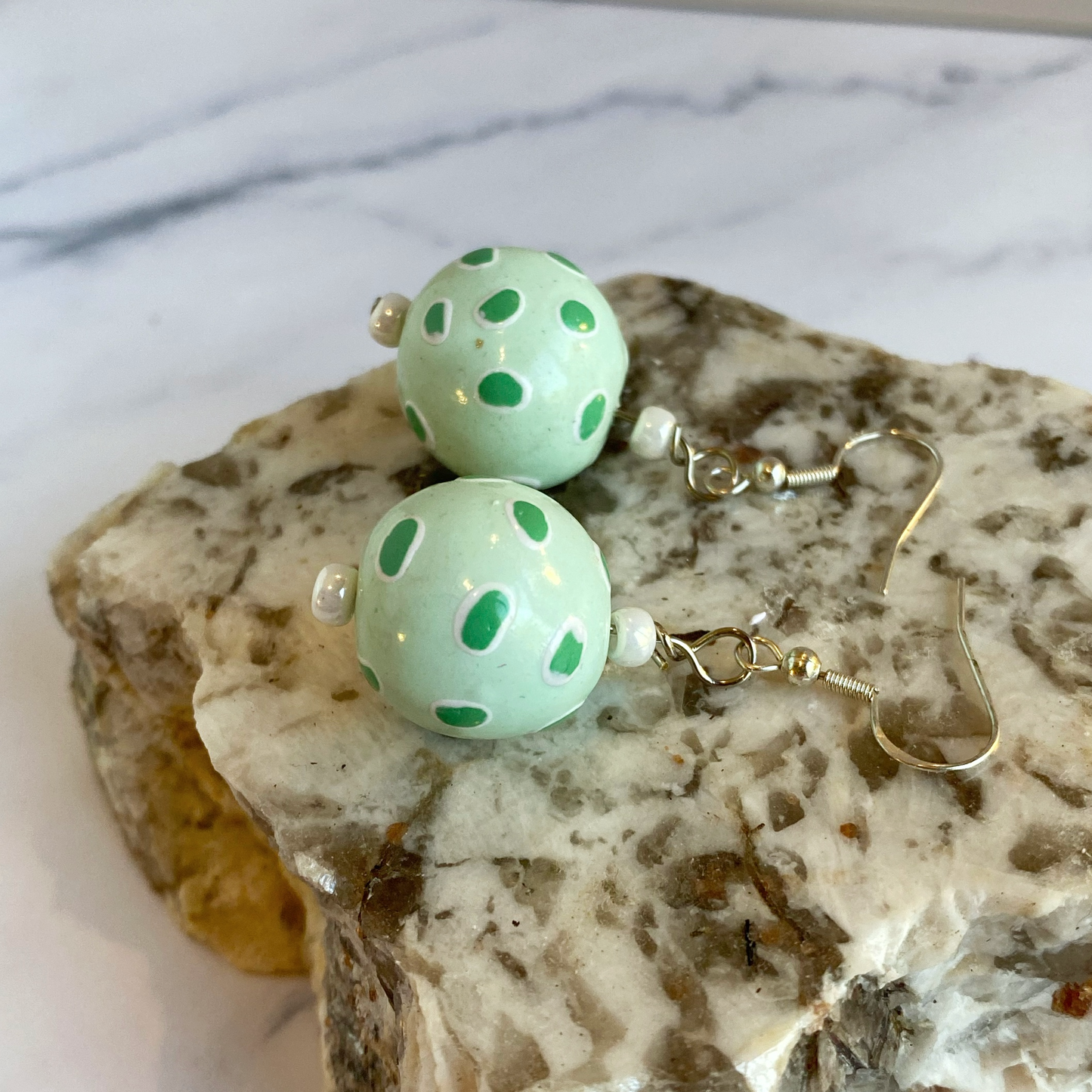 Pair of light green earrings with polka dots on a marble surface