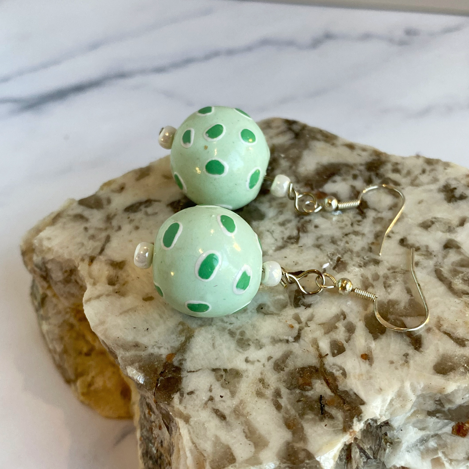 Pair of light green earrings with polka dots on a marble surface