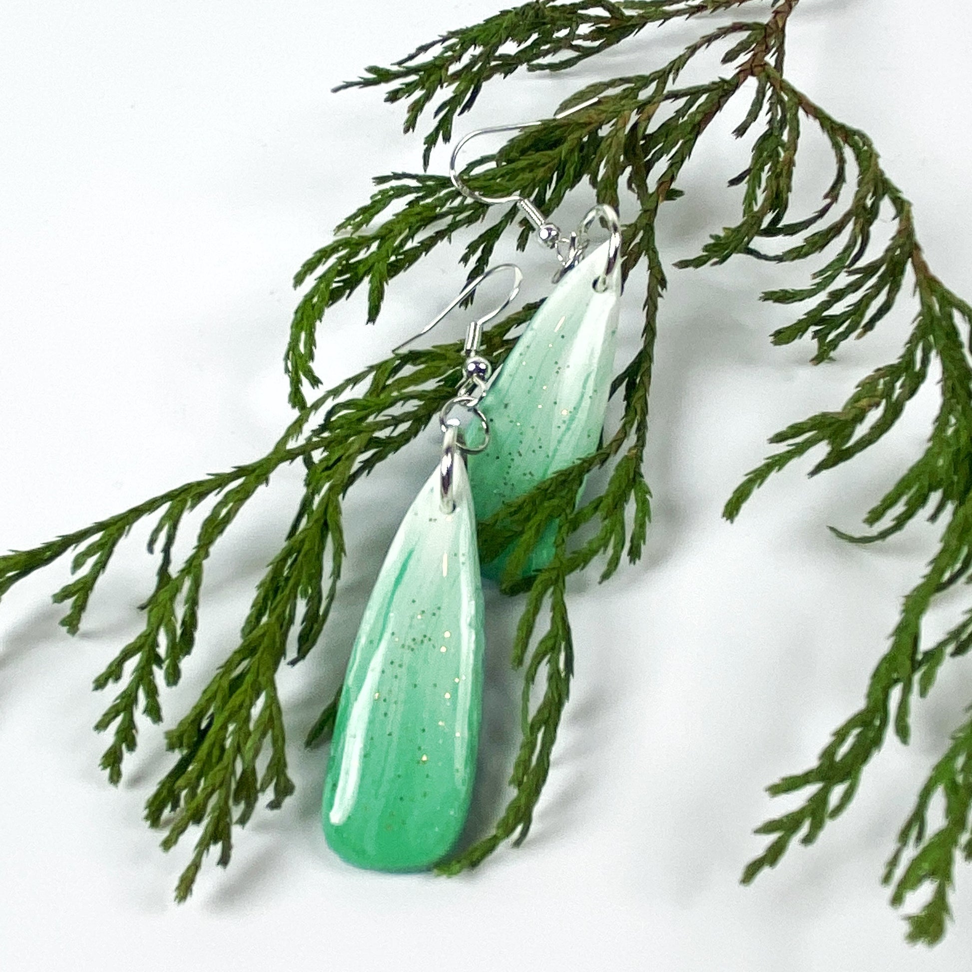 Green Aurora Polymer Clay Handmade Dangle Earrings front view with greenery