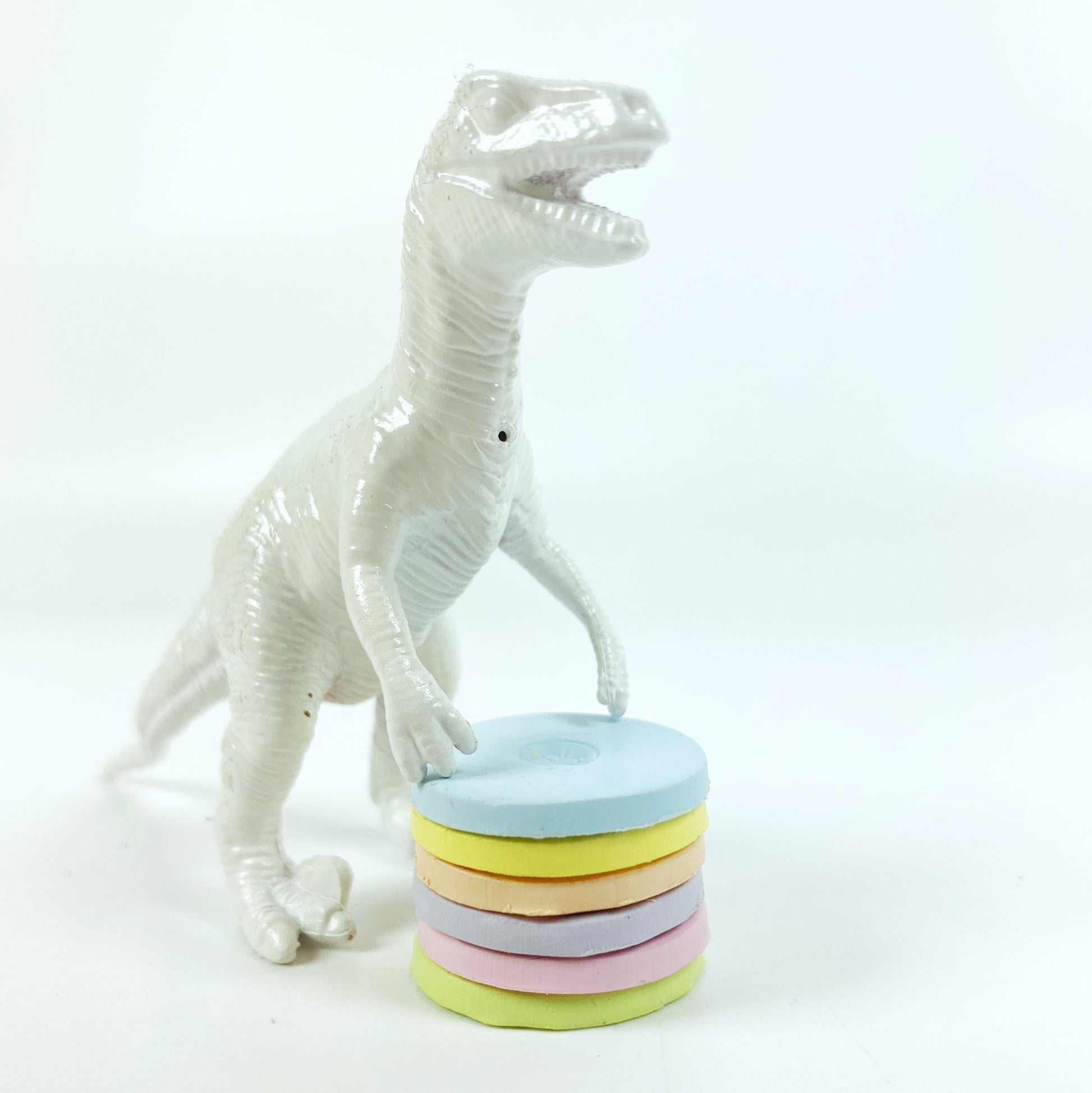 A stack of 6 polymer clay color sample discs with a white dinosaur presiding.