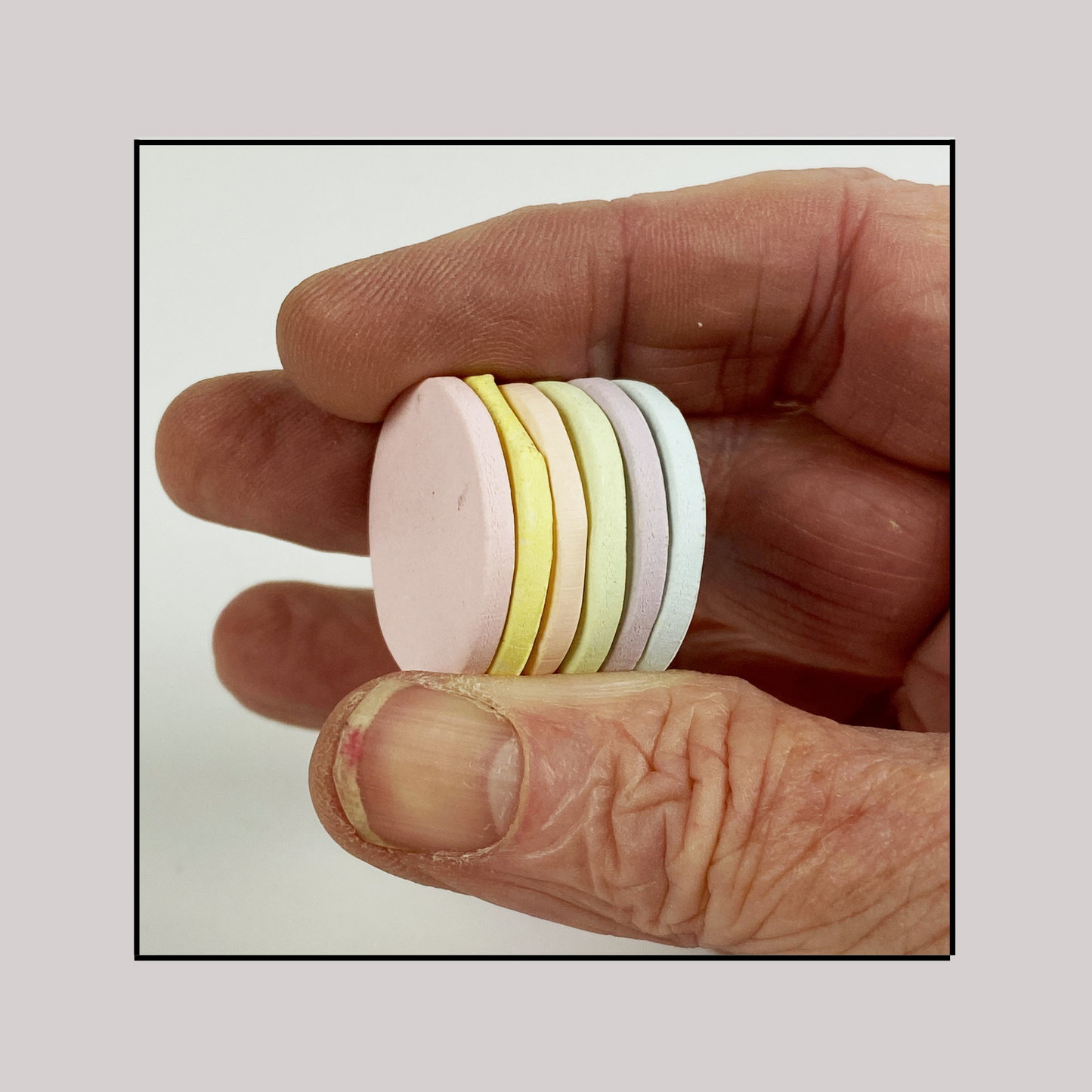 Polymer ClayPale Dawn Color Palette. Stacked sample discs of each clay color, held in a hand for a side view.