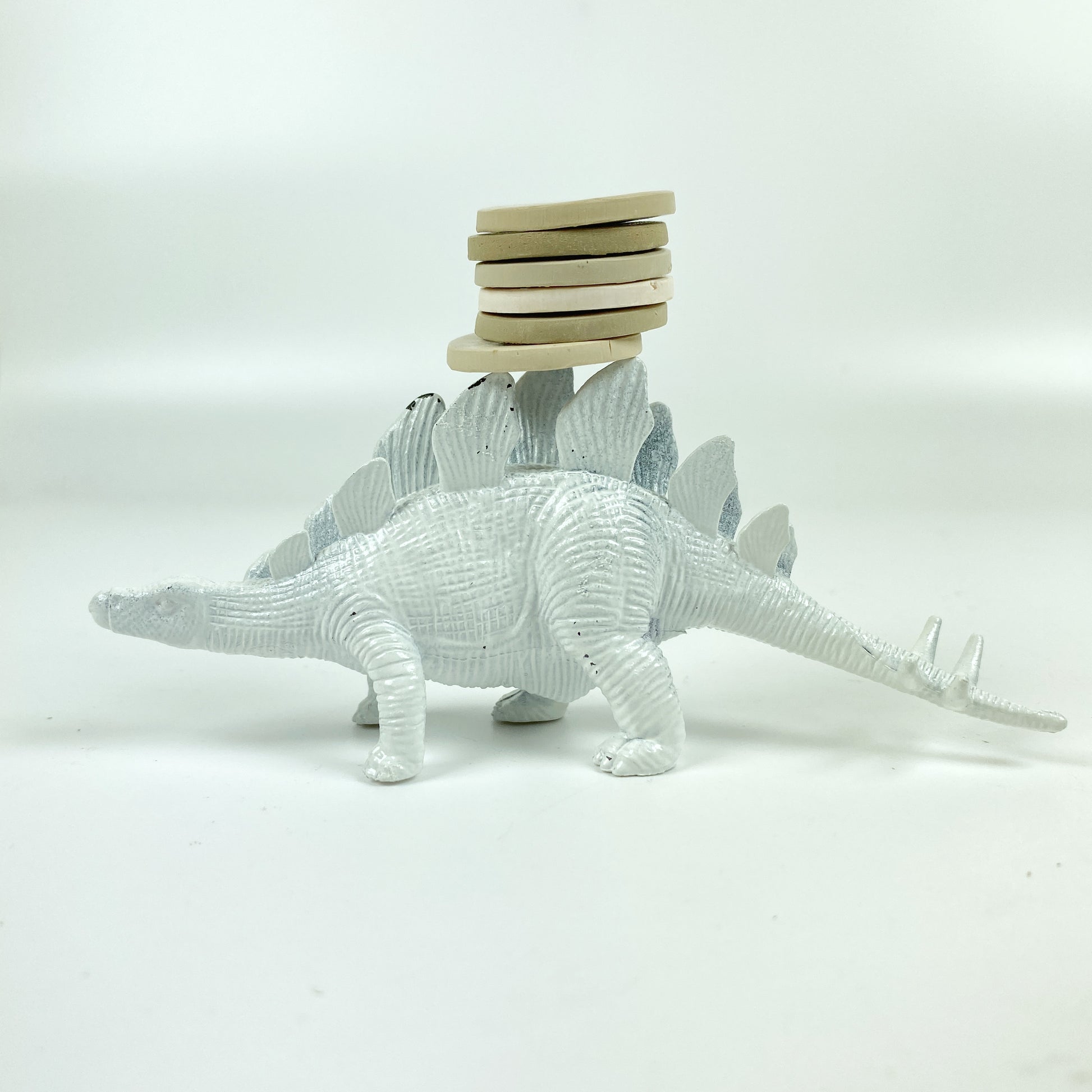 A stack of 6 polymer clay color sample discs with a white dinosaur carrying them..